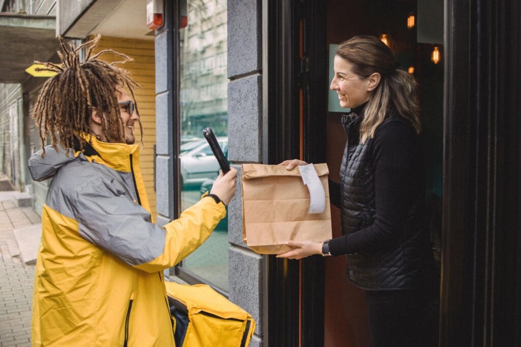 Restaurant staff handing a takeout order to a food delivery driver for online delivery service.